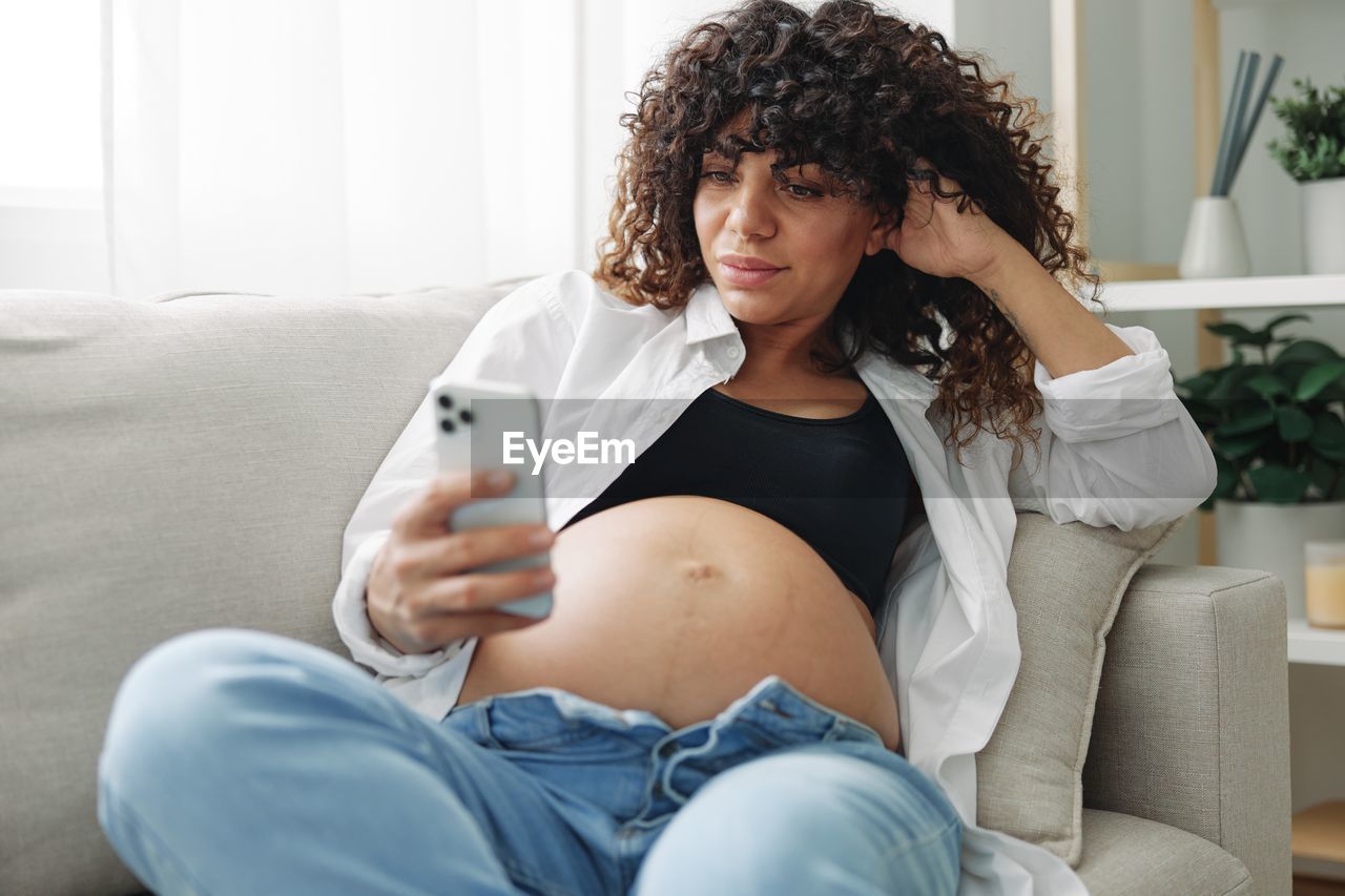 portrait of young woman using mobile phone while lying on sofa at home