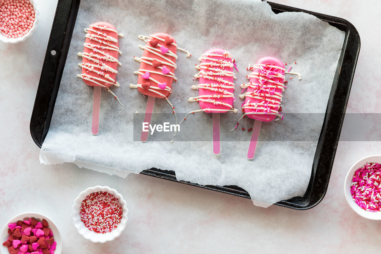 Valentine cakesicles decorated with candy melt drizzle and sprinkles.