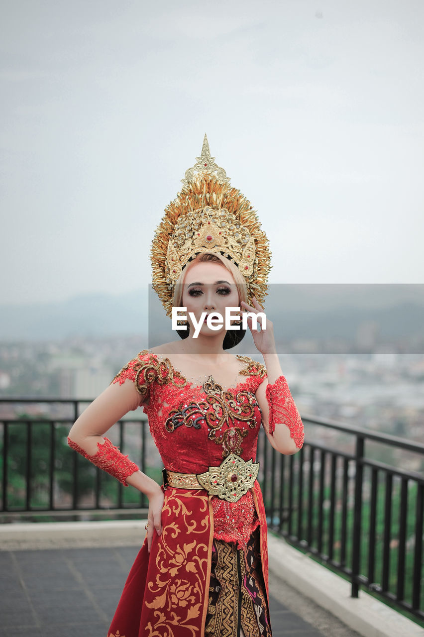 Woman with custome traditional of bali  standing by railing against clear sky