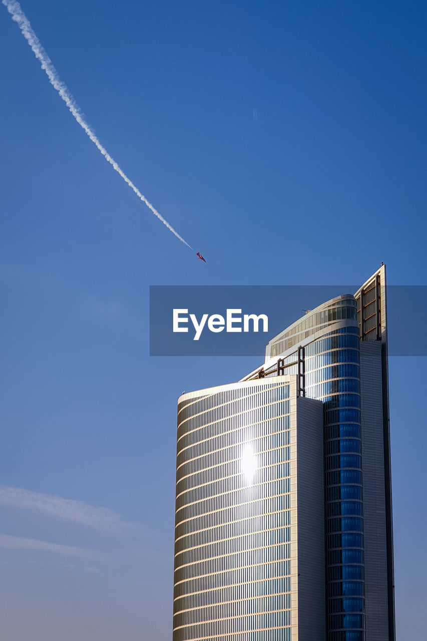 Low angle view of a skyscraper against blue sky and an airplane doing an airshow in abu dhabi uae. 