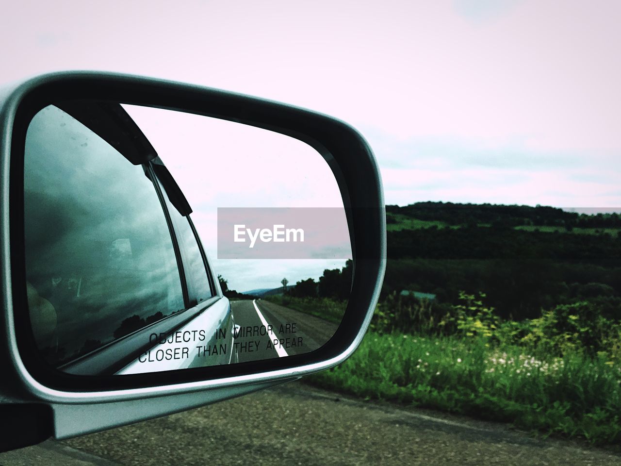 Close-up of side-view mirror over road against sky