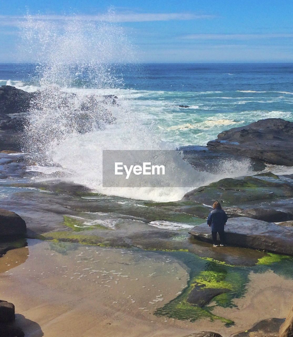 High angle view of woman looking at waves breaking against rock on beach