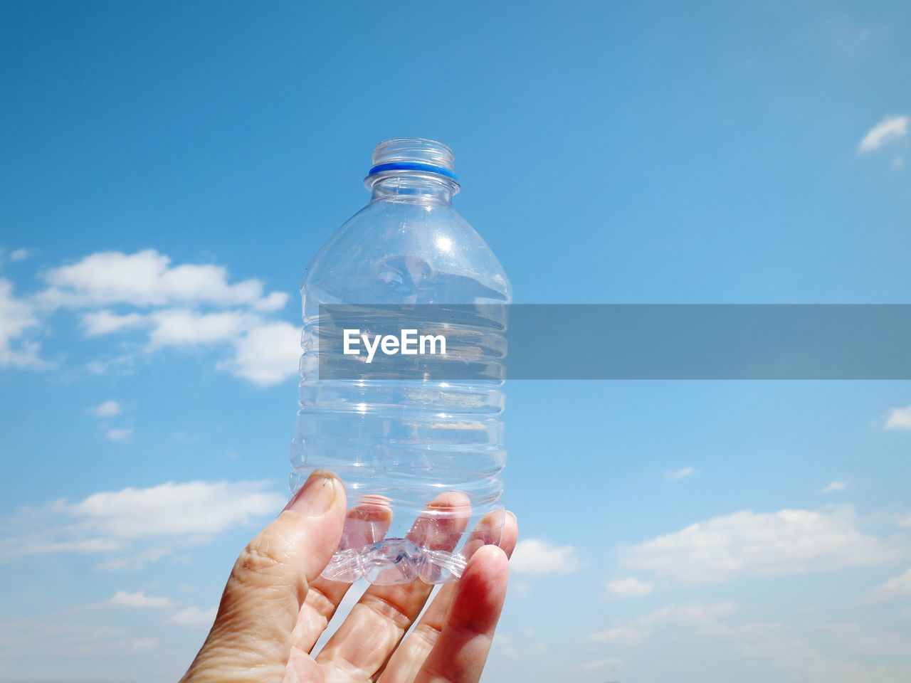 Close-up of hand holding plastic bottle against sky