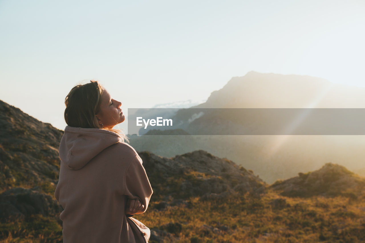 Thoughtful young woman on mountain peak against sky