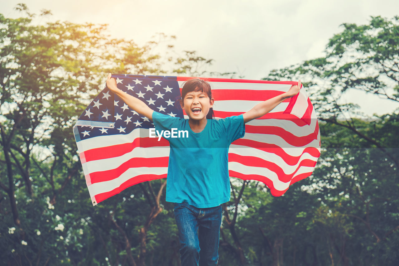 Happy teenage girl with american flag against trees