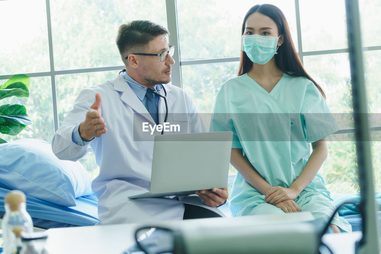 Doctor using laptop talking with patient in hospital