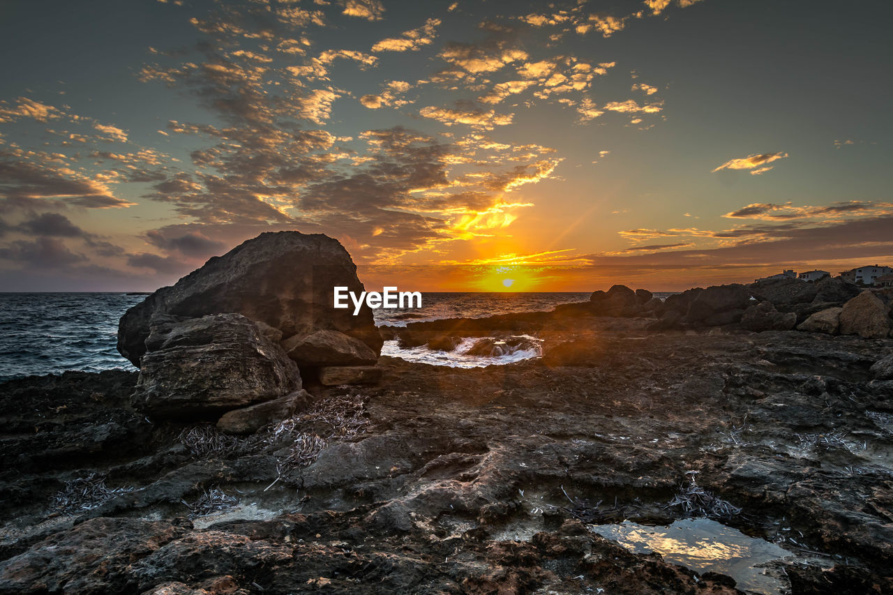 Rock formation in sea against sky during sunset