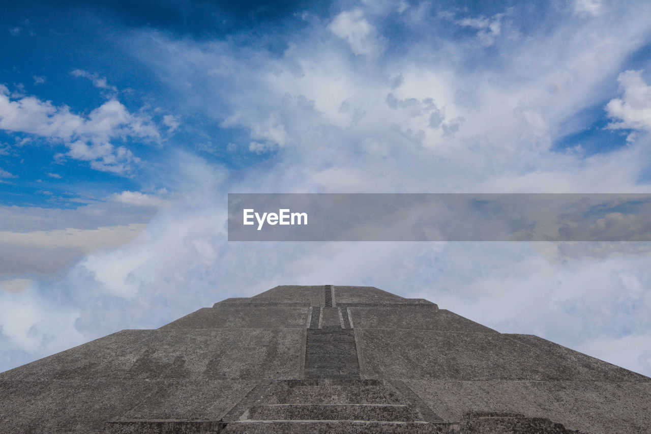 Low angle view of pyramid against cloudy sky
