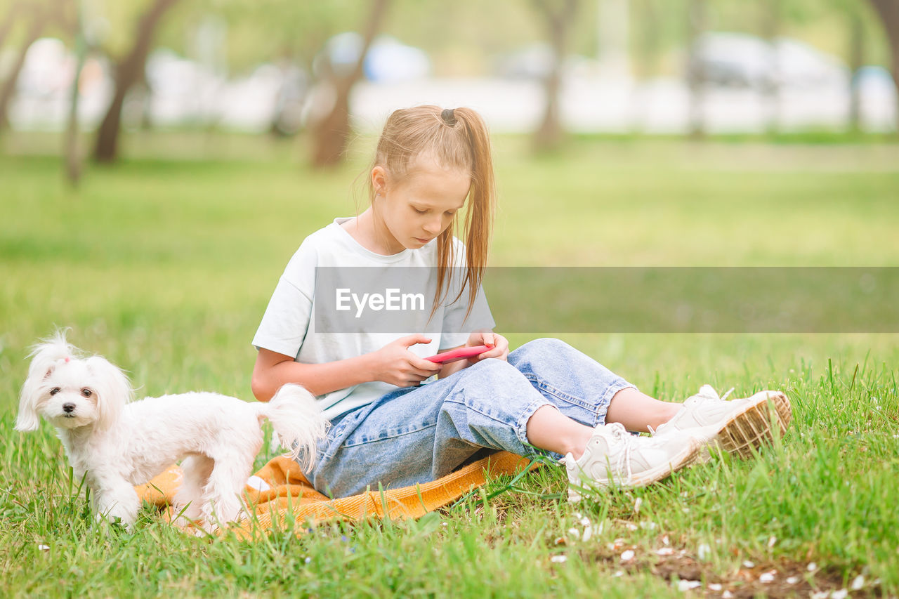 Full length of girl using phone with dog outdoors