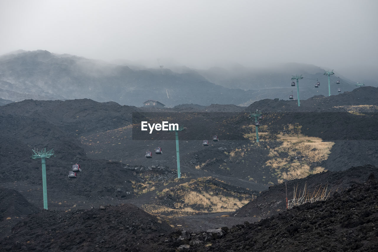View of cable cars moving over volcanic landscape of mount etna covered in smoke