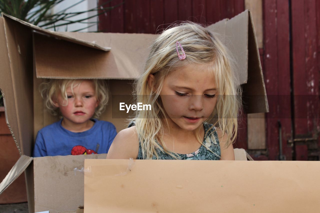 Cute boy and girl looking away while sitting in boxes