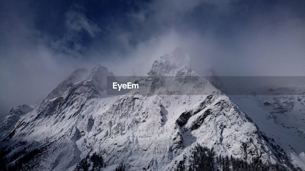 Low angle view of snowcapped mountain against sky in foggy weather