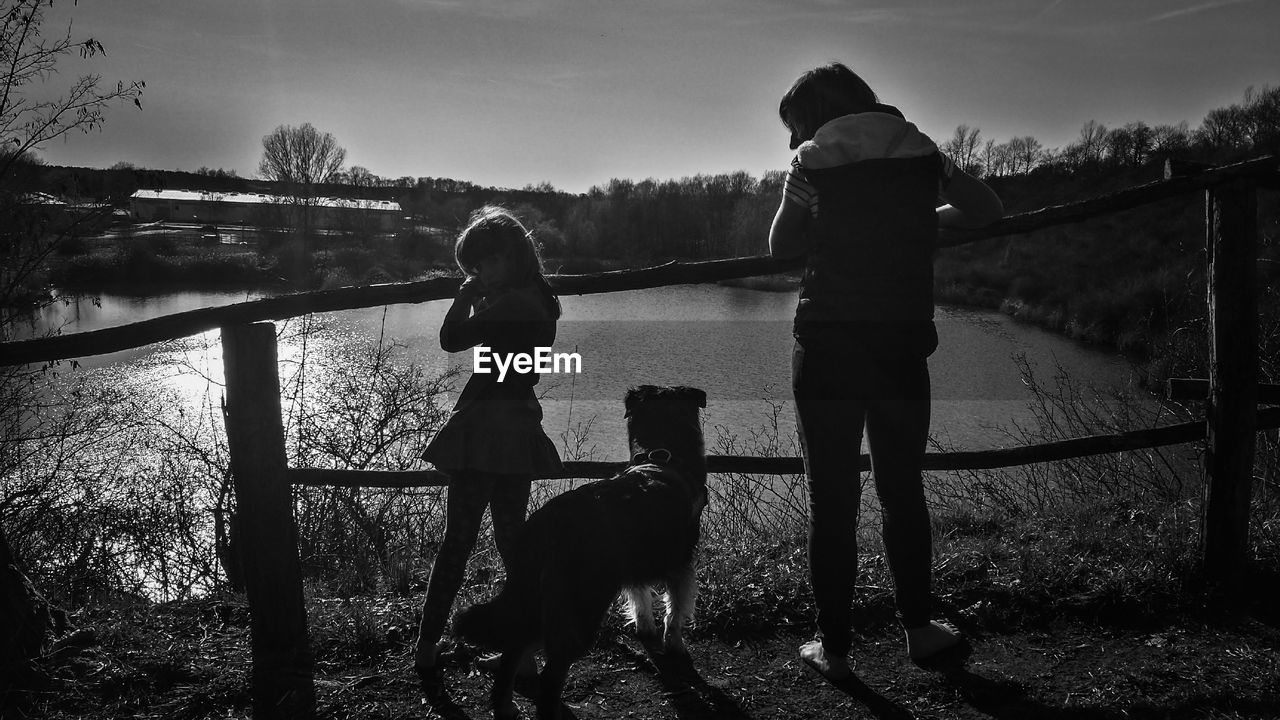 REAR VIEW OF WOMAN WITH DOG STANDING BY WATER