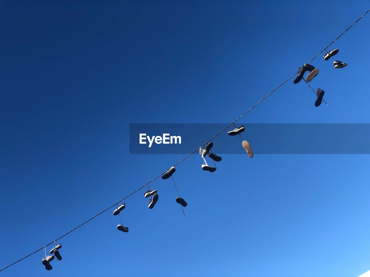 Low angle view of shoes on cable against clear blue sky