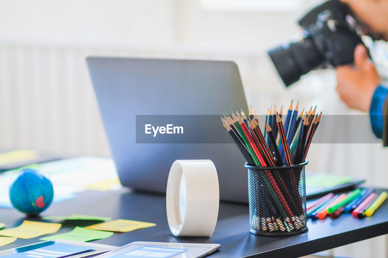 Close-up of colored pencils with laptop and papers on table