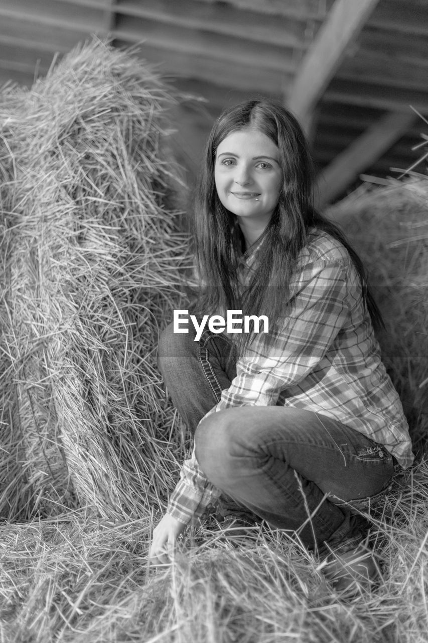 Black and white portrait of young woman sitting on hay bale