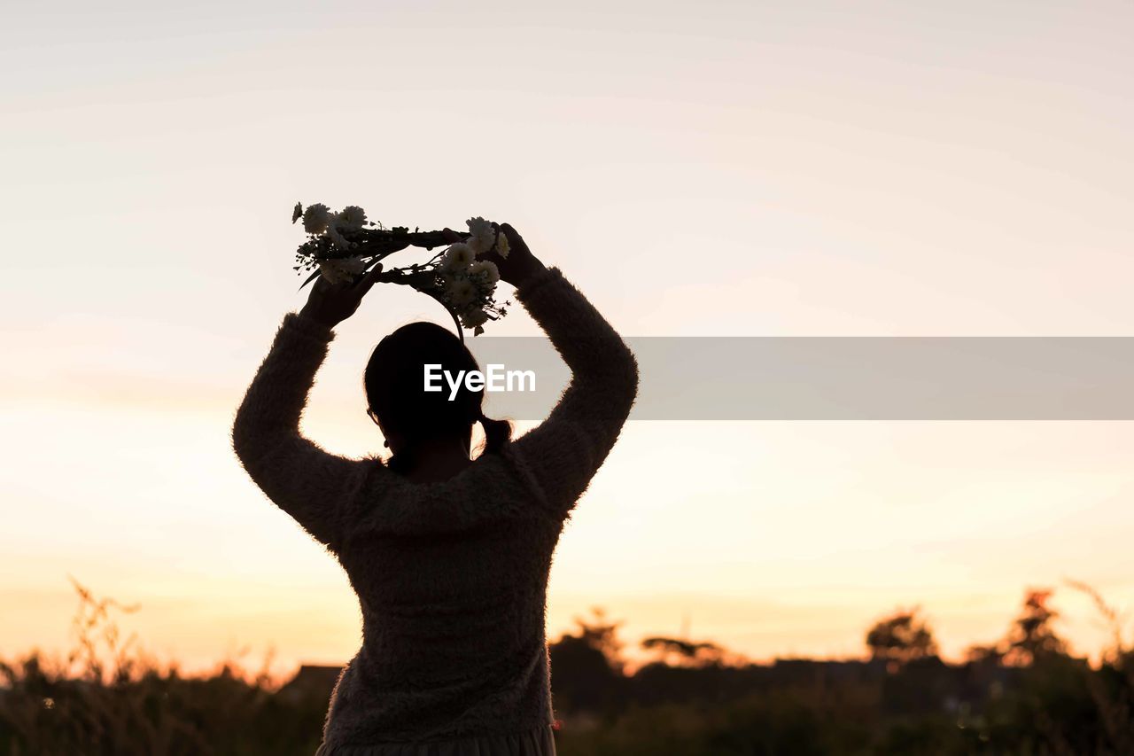 Rear view of woman standing on field against sky during sunset