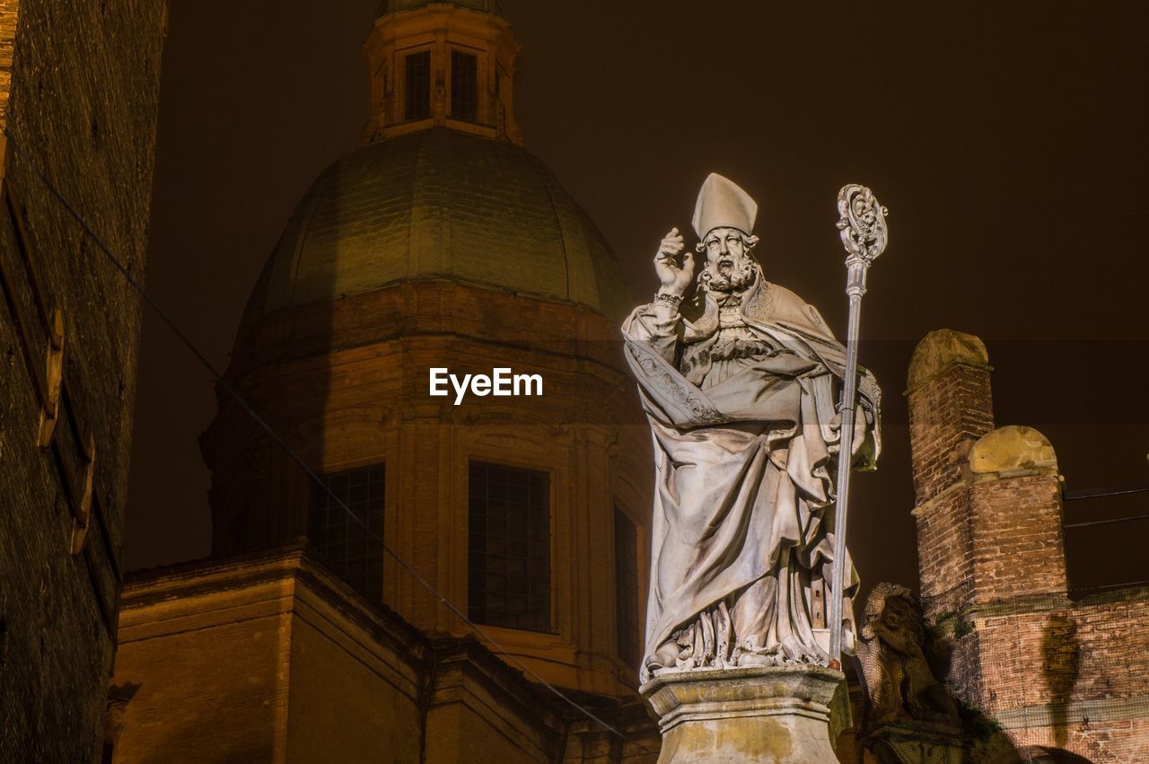 Low angle view of statue against church at night