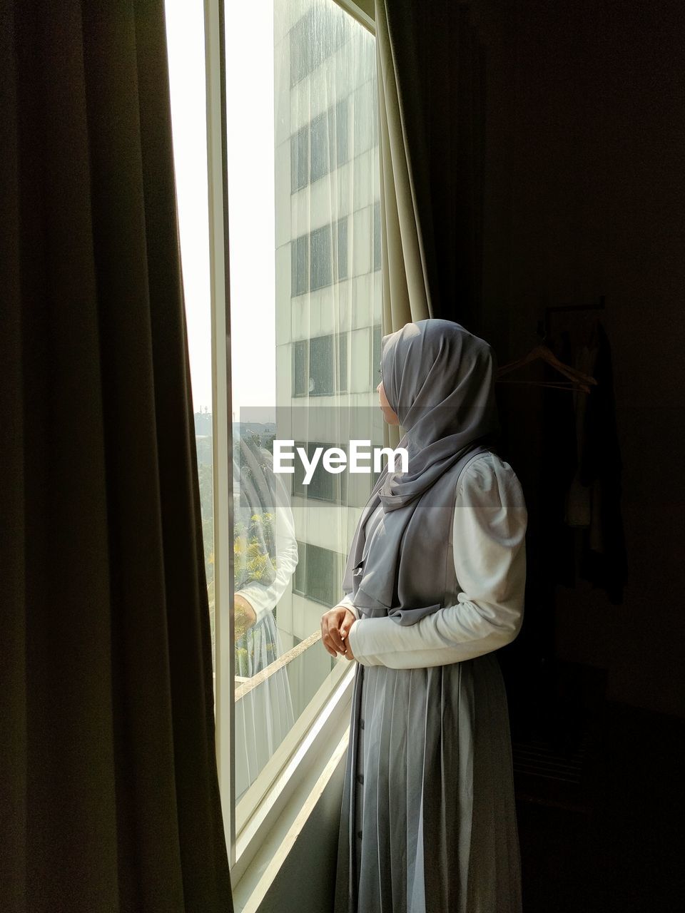 Side view of woman standing by window at home