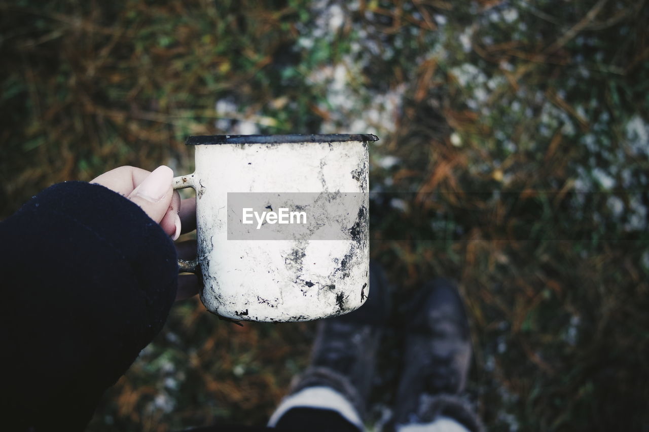 Close-up of woman hand holding dirty mug on field