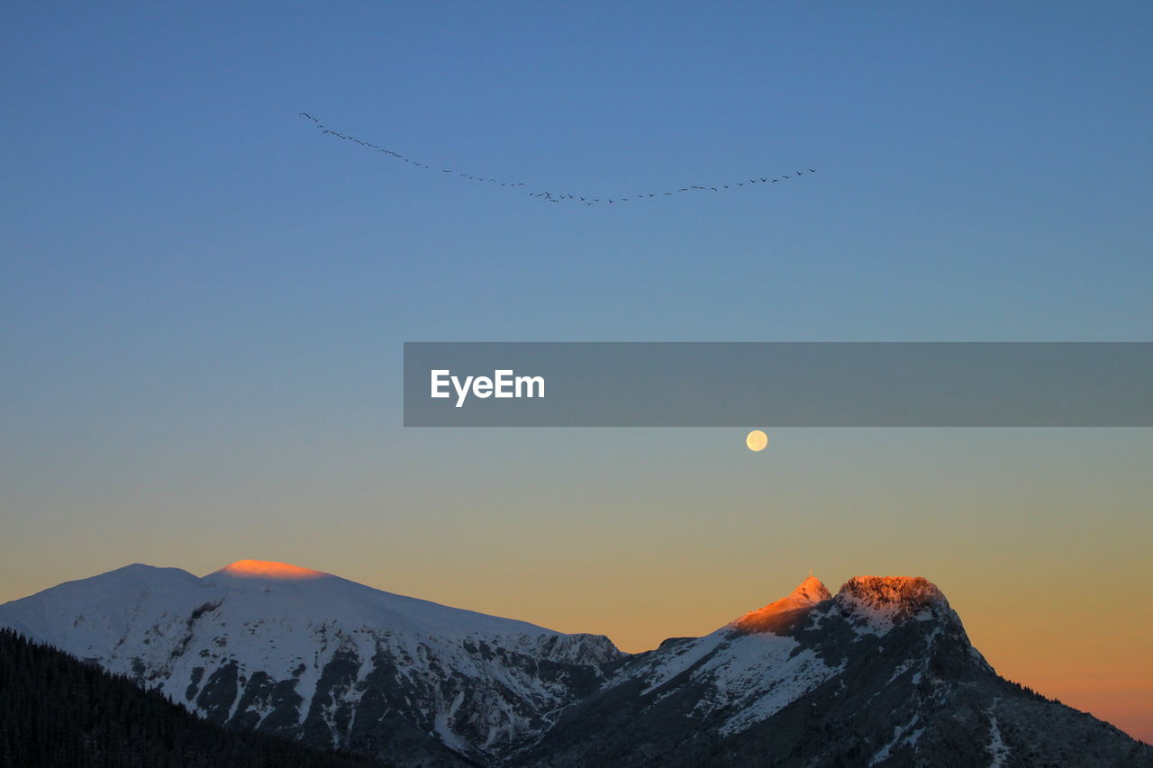 Scenic view of snowcapped mountains against clear sky during sunrise