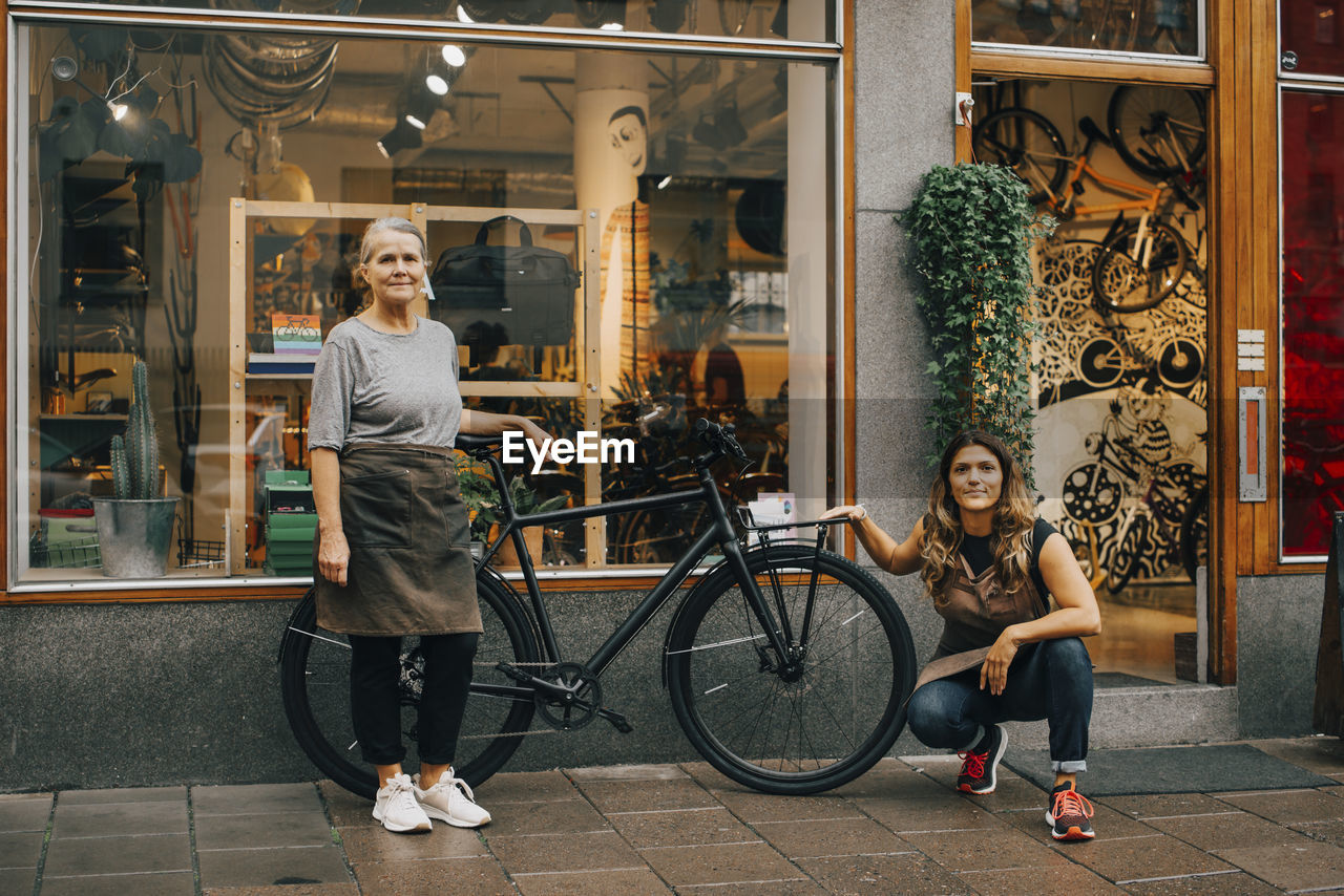 Portrait of female coworkers by bicycle outside repair shop