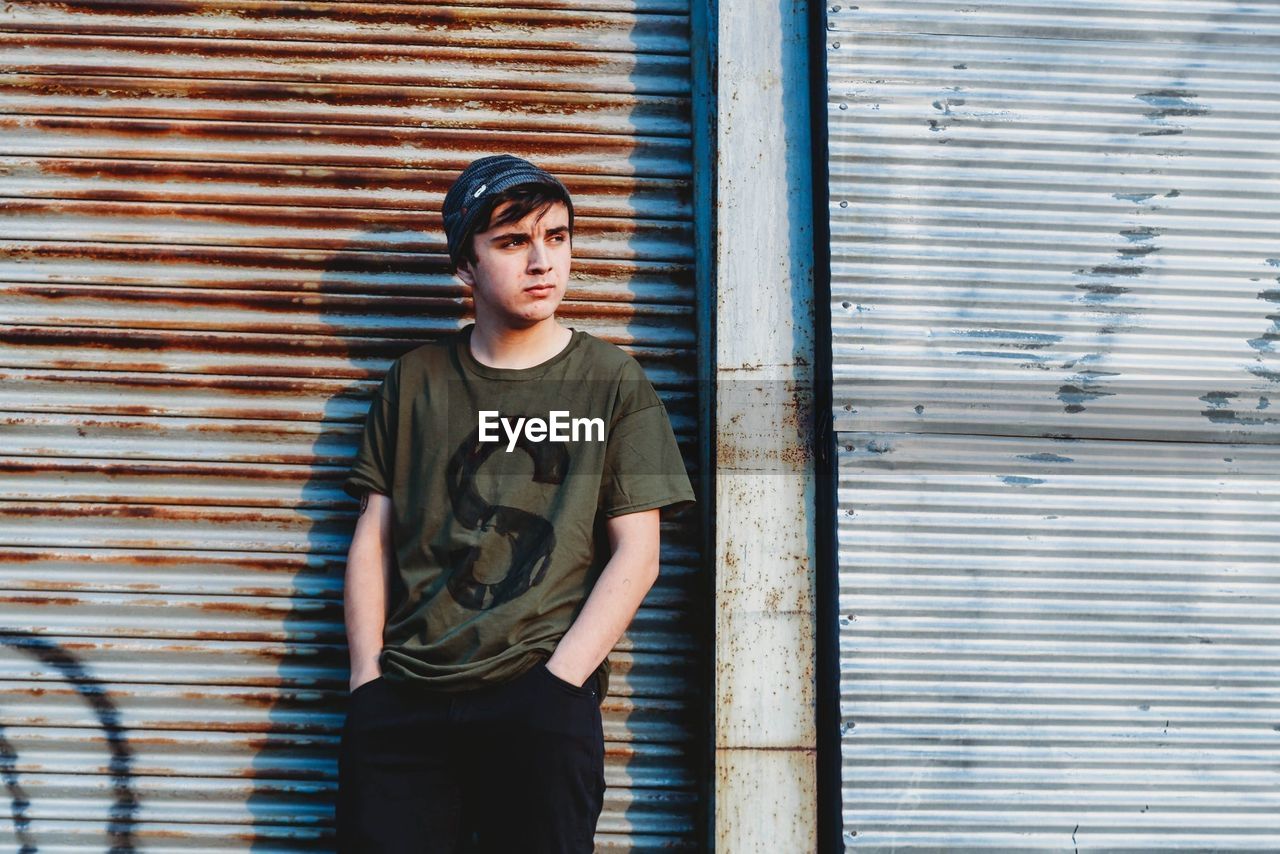 Thoughtful teenage boy standing against closed shutter