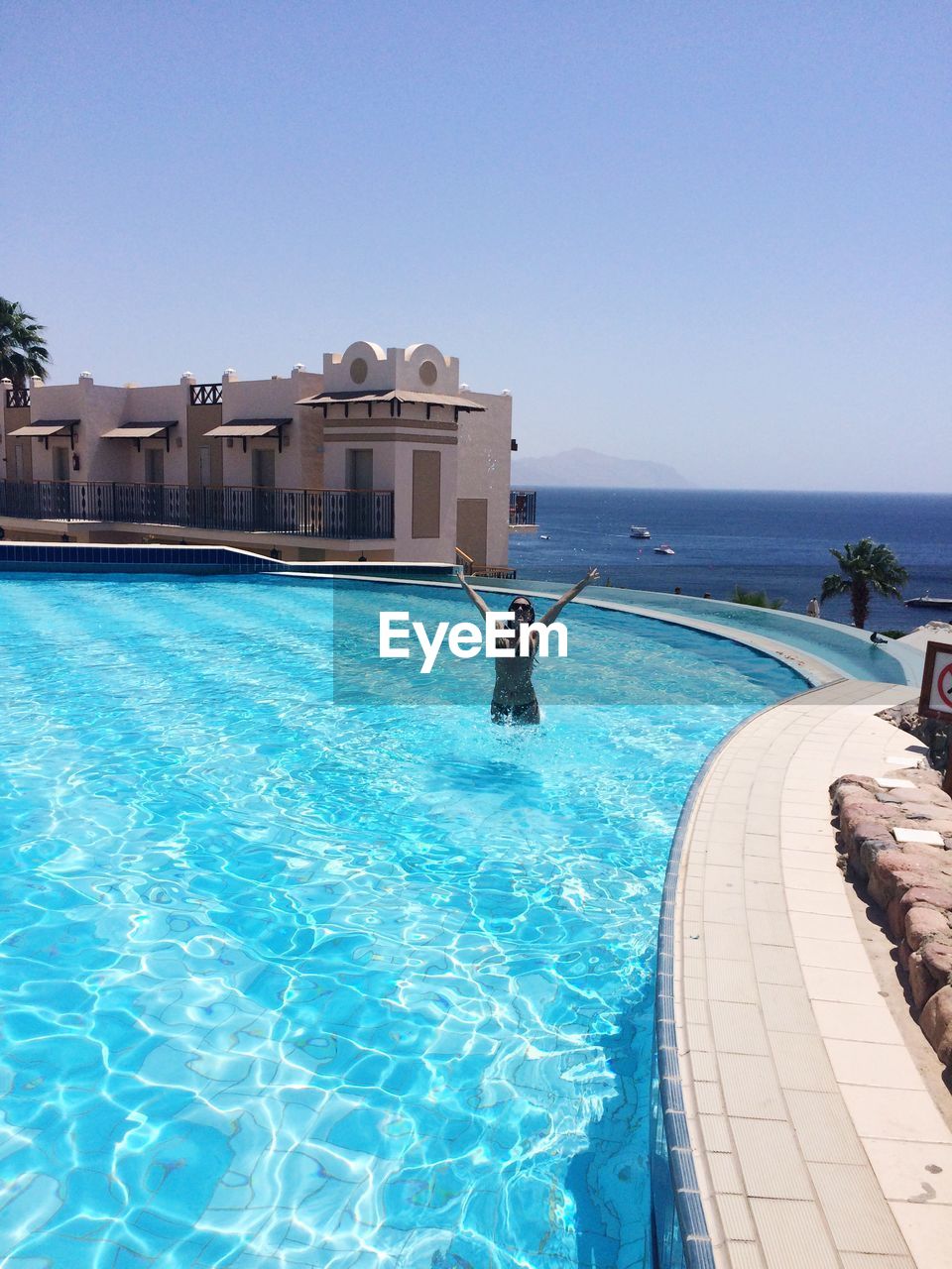 VIEW OF SWIMMING POOL BY SEA AGAINST CLEAR BLUE SKY