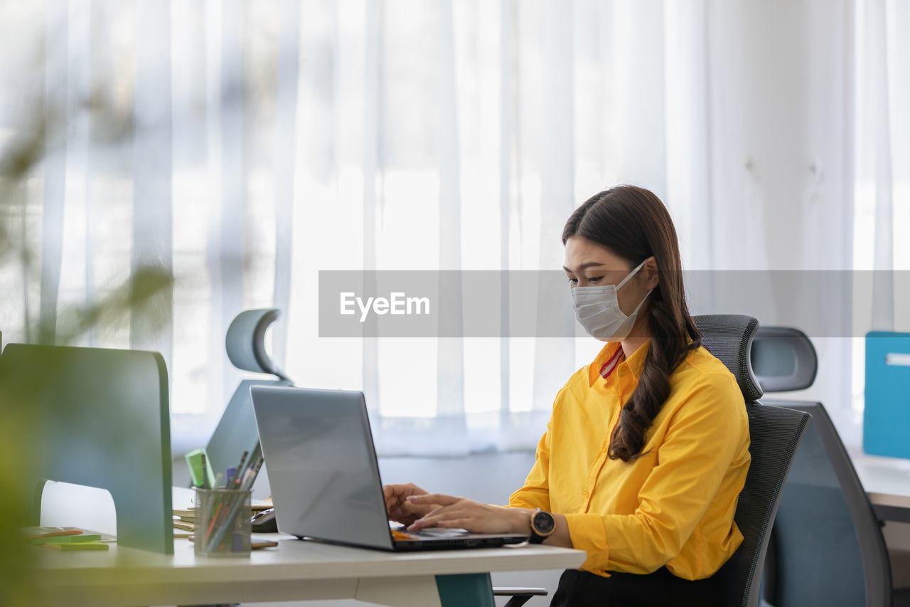 Woman wearing mask while sitting by laptop on table