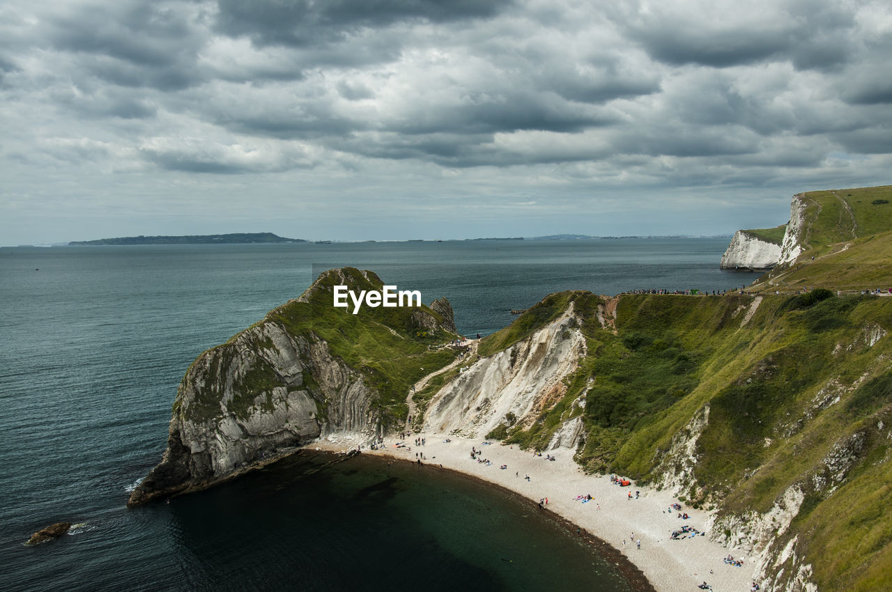 Mossy mountains by sea against cloudy sky at durdle door