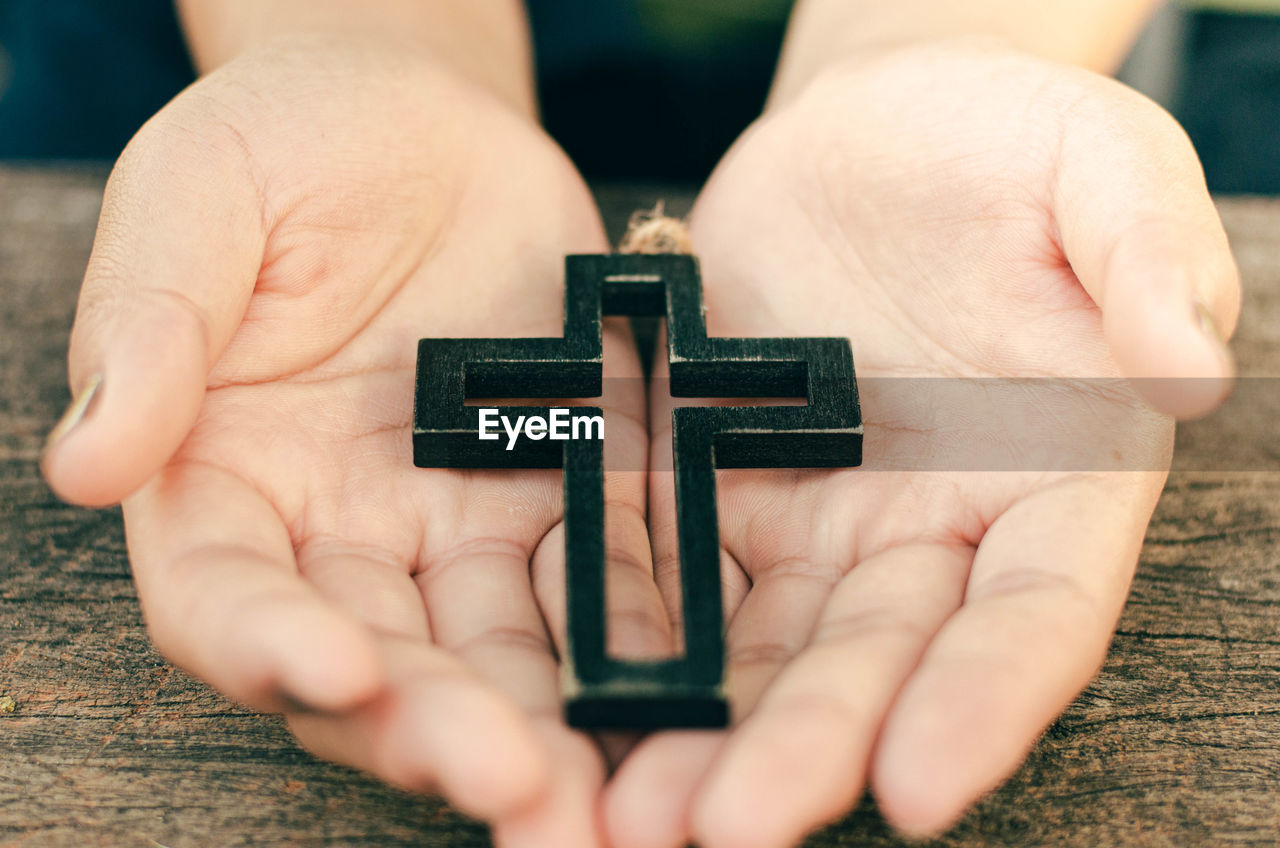 Cropped hands of person holding religious cross over table
