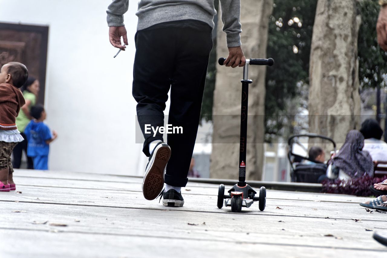 Low section of man carrying push scooter on wooden footpath