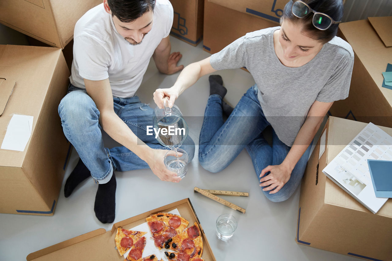 Woman serving water to man while having pizza during relocation of new house