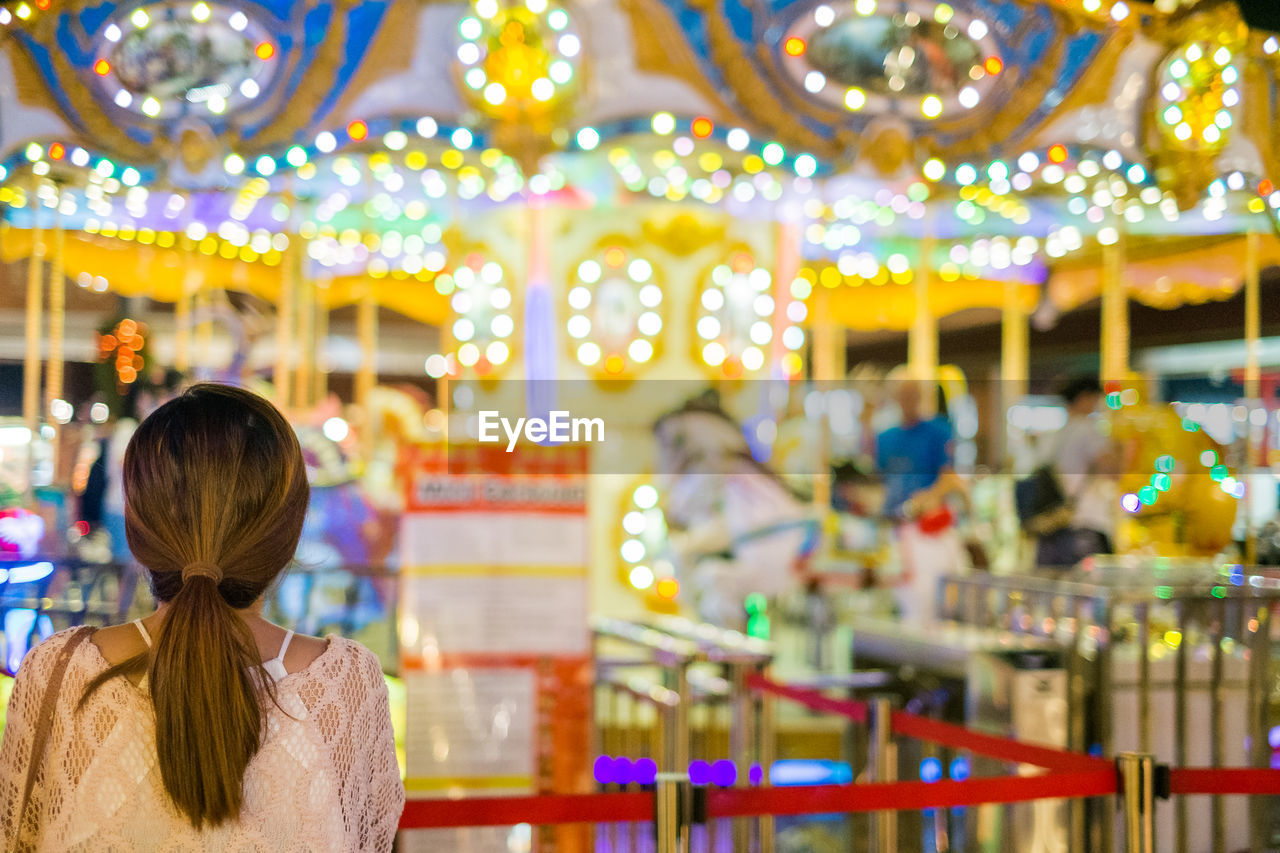 Rear view of woman looking at illuminated carousel at night