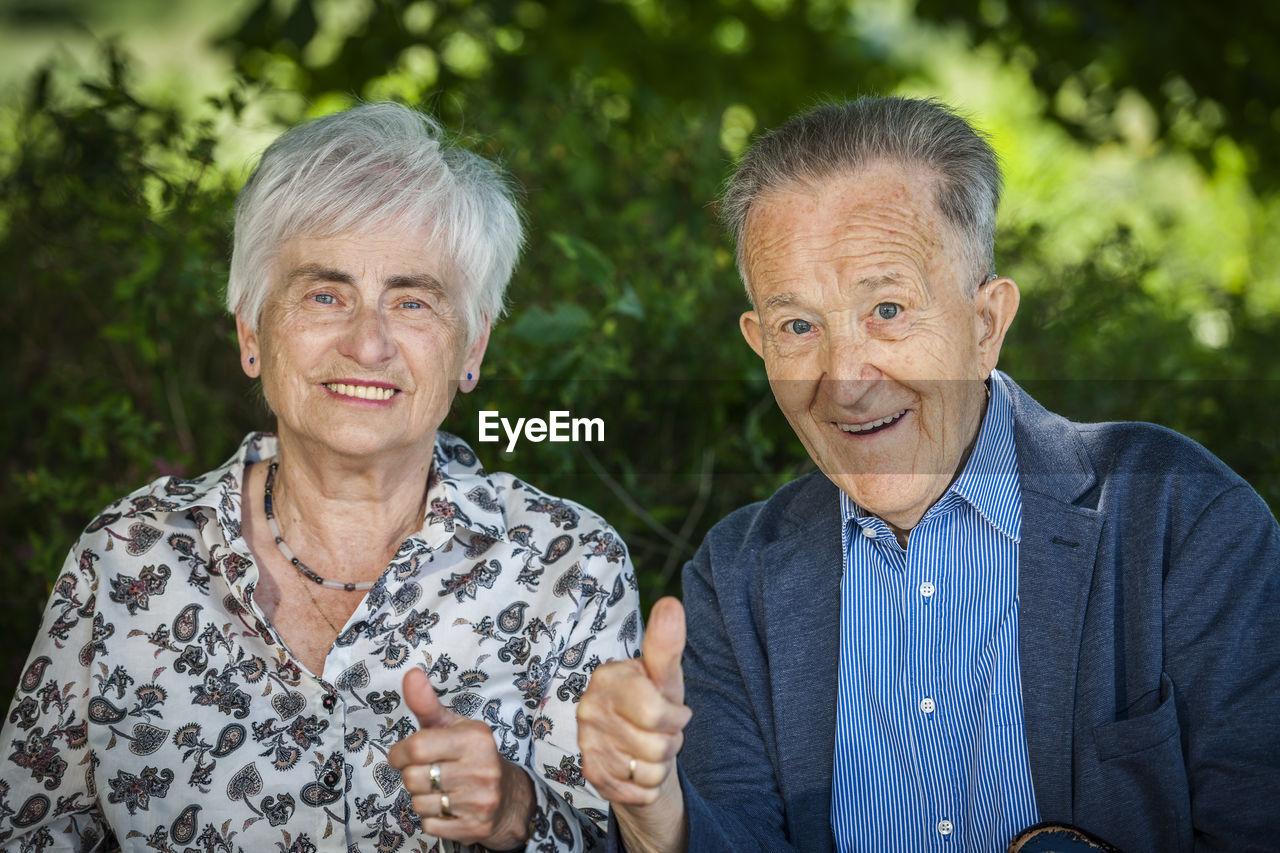 Portrait of an 80 year old retired couple showing the thumbs up and friendly looking at the camera.