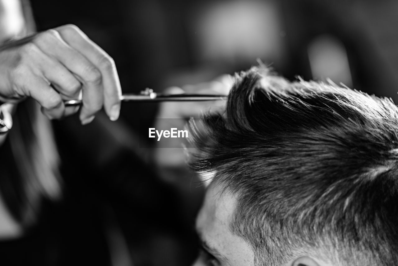 Cropped hand of woman cutting man hair at shop