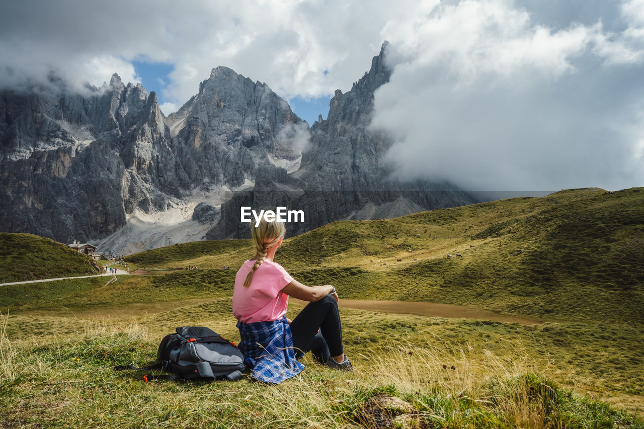 REAR VIEW OF WOMAN SITTING ON LAND AGAINST MOUNTAIN