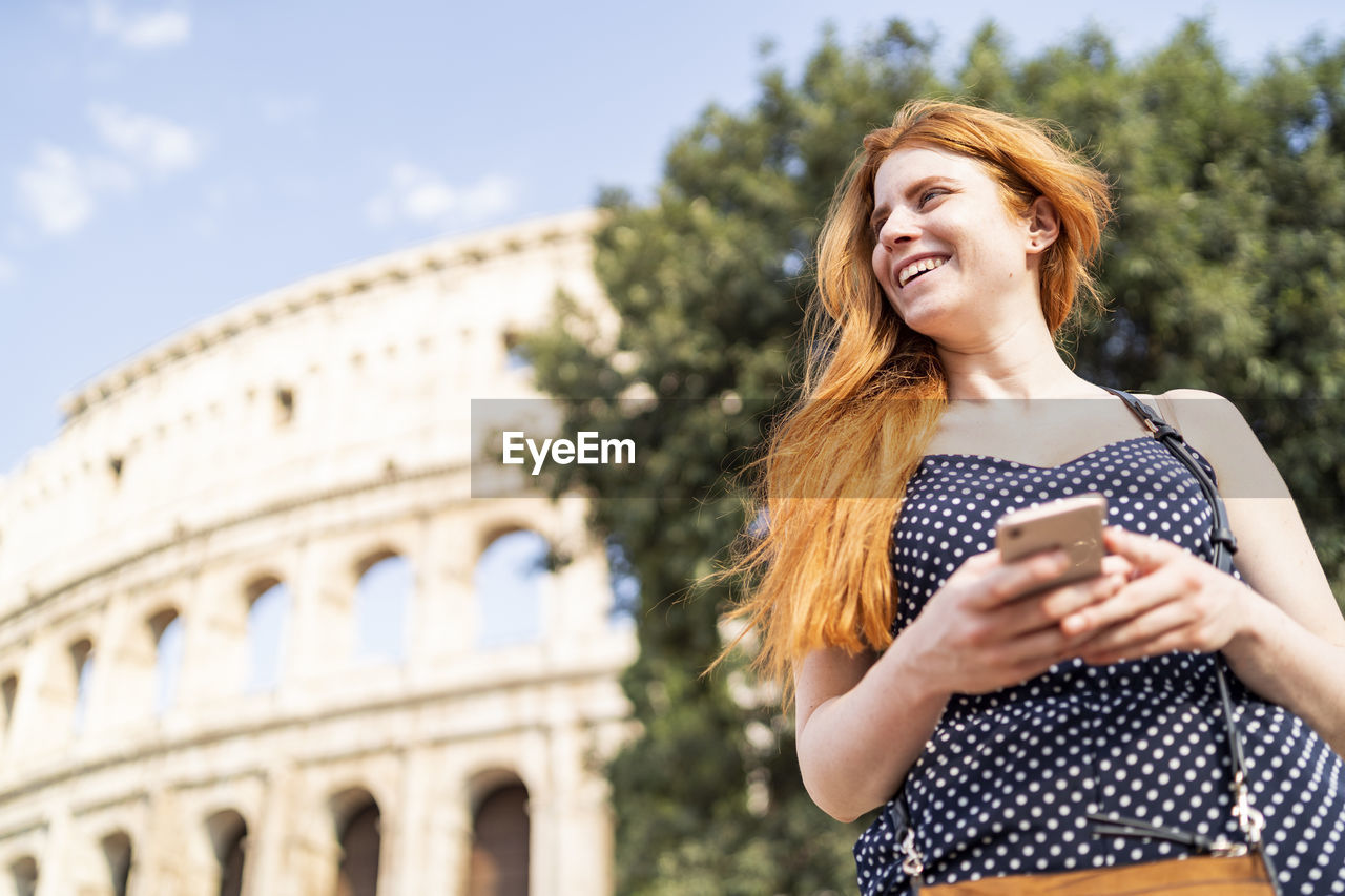 Optimistic ginger tourist browsing smartphone on sunny day