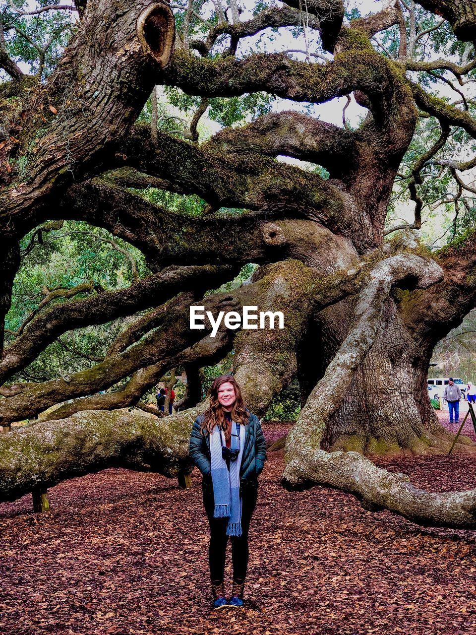 FULL LENGTH PORTRAIT OF YOUNG WOMAN STANDING AGAINST TREE