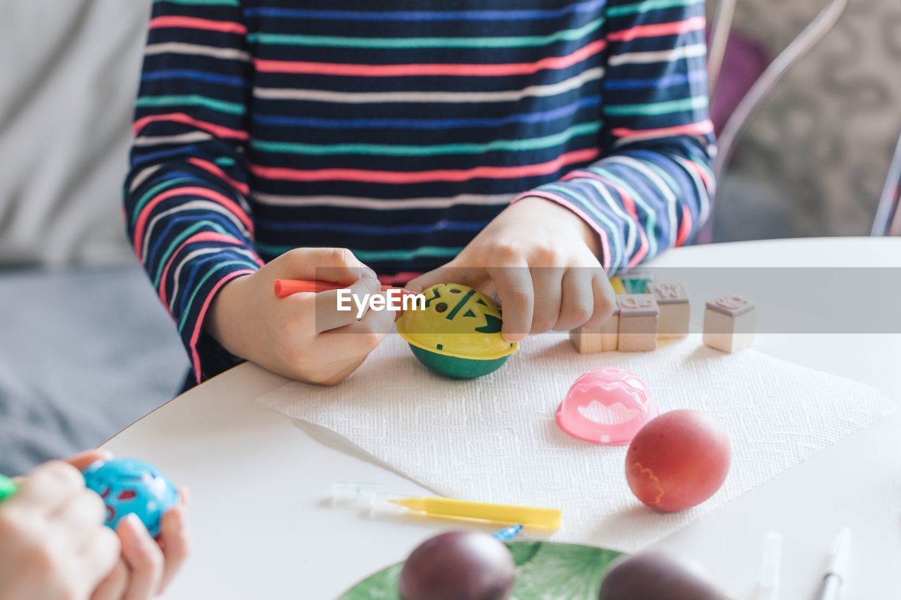 Close-up of siblings drawing on easter eggs at table