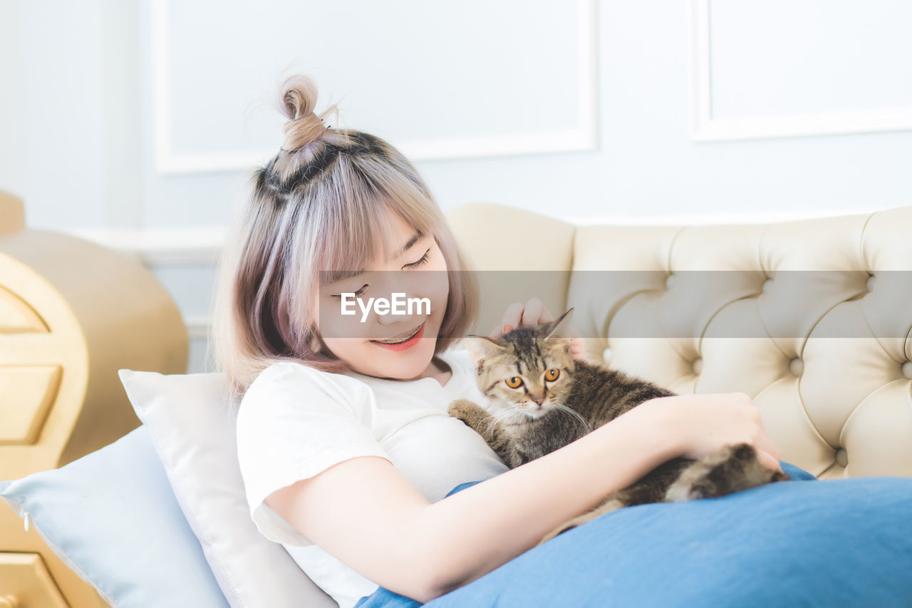 Smiling woman playing with cat while lying on sofa at home
