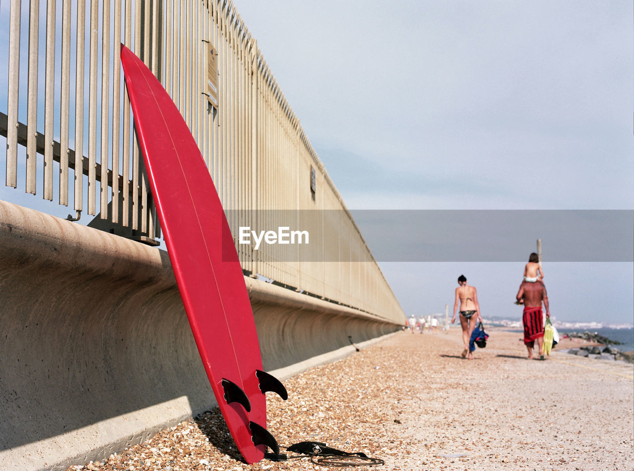 Red surfboard at beach against sky