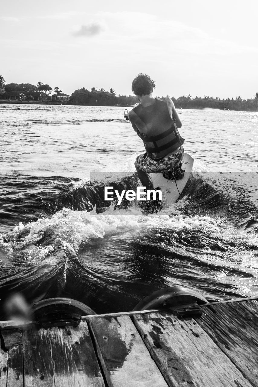 Rear view of man wakeboarding by pier on sea