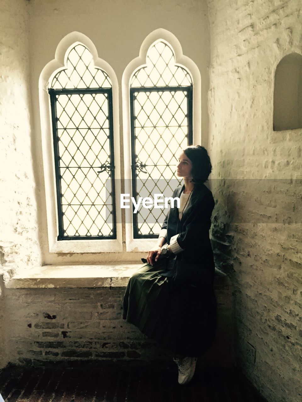 Young thoughtful woman sitting on window sill at home