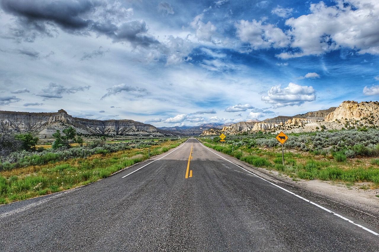 Empty road on field by mountains against sky