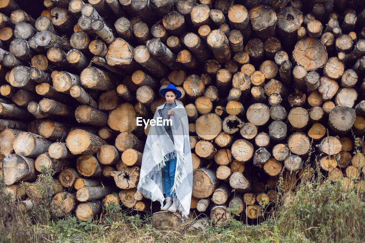 Woman director is standing by a log at a sawmill in a scarf and a blue hat in autumn