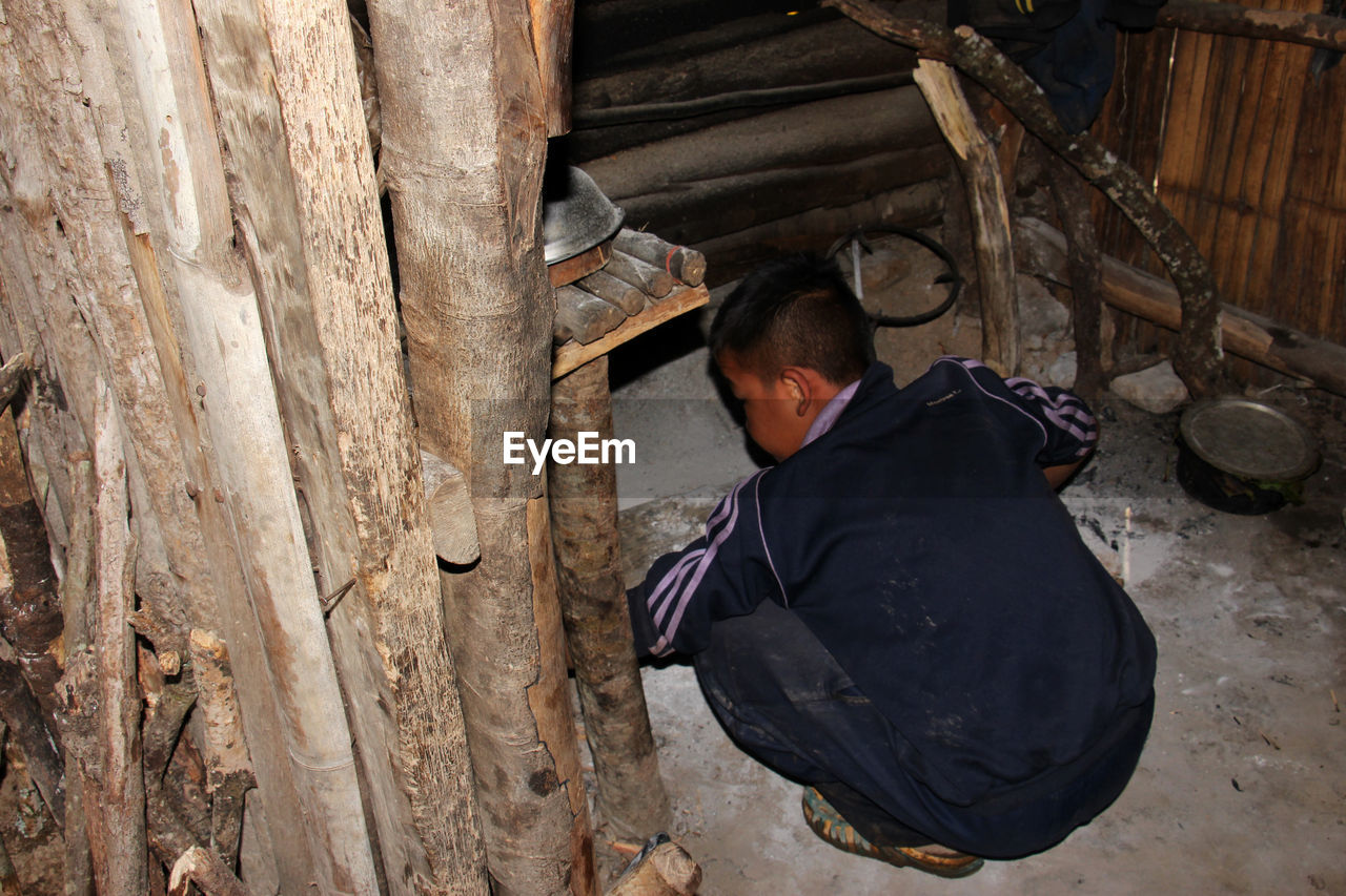 HIGH ANGLE VIEW OF MAN SITTING AT WOOD