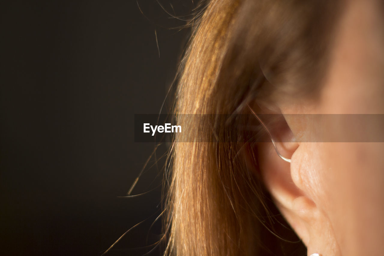 Close-up of woman wearing hearing aid against black background