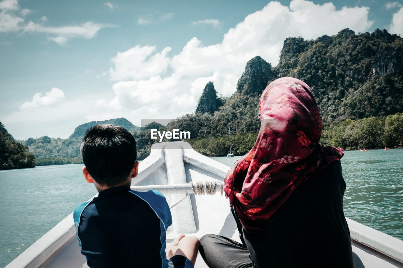 Rear view of siblings sitting on boat sailing against river