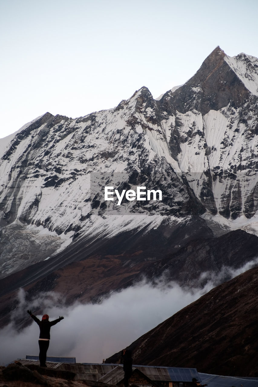 Rear view of woman with arms outstretched standing by snowcapped mountain